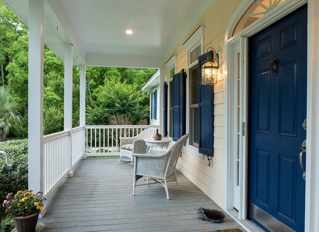 Personal Insurance - Closeup View of the Front Porch of a Colonial Southern Style Home with Two White Chairs and Green Foliage Surrounding the House